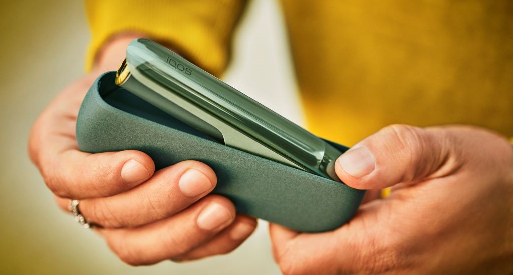 Podgrzewacz IQOS ILUMA w otwartej przenośnej ładowarce w zielonym odcieniu