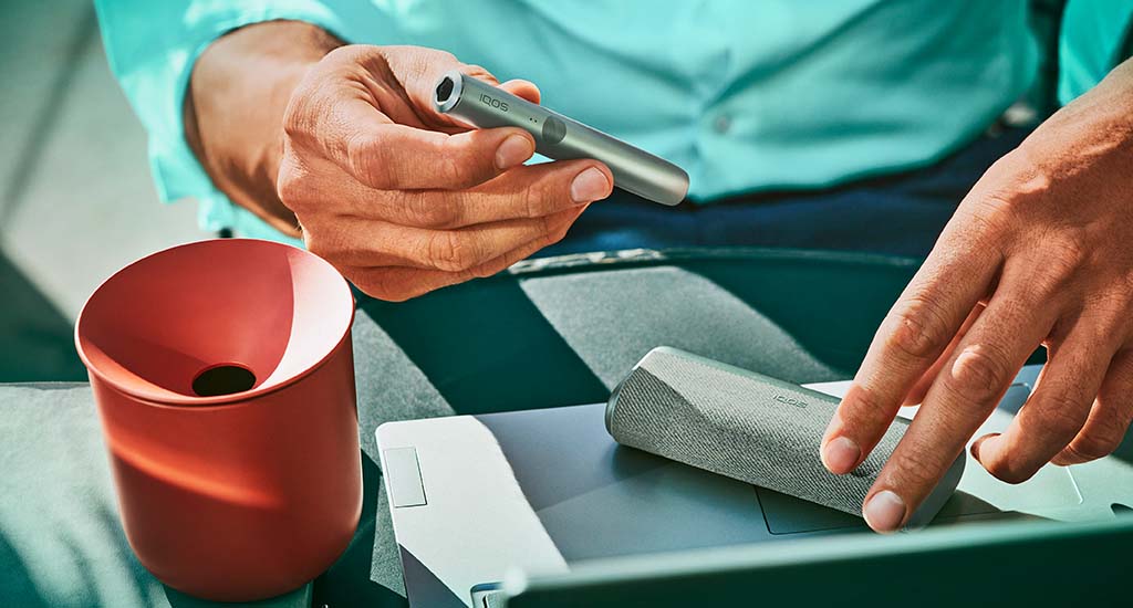 Podgrzewacz IQOS ILUMA PRIME w zielonym odcieniu i pojemnik na zużyte wkłady tytoniowe w czerwonym odcieniu